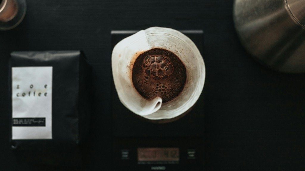 Overhead pour-over cup, coffee bag, and kettle on a dark counter.